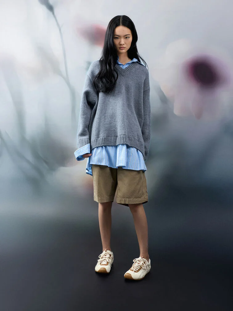 An oversized button-up shirt layered with an oversized sweater and paired with jorts.