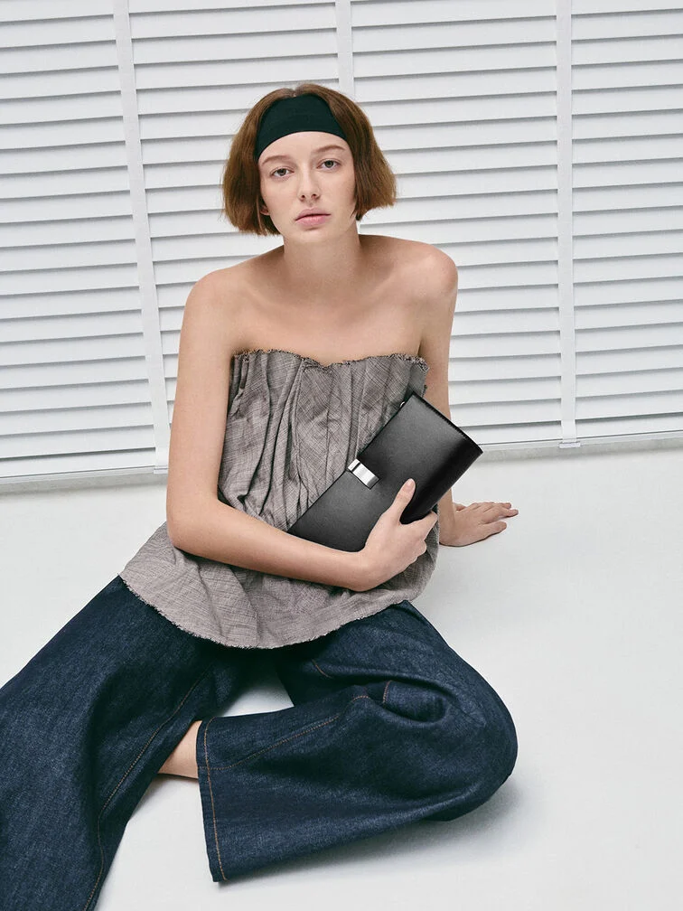 Clutch yang digenggam dengan mantap dari bawah menggunakan ibu jari di depan dan jari-jari lain di bawahnya, cara memegang yang praktis namun tetap anggun.